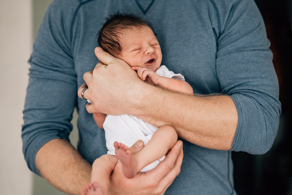 A close up photo of a newborn  being held facing out in front of his father's chest.