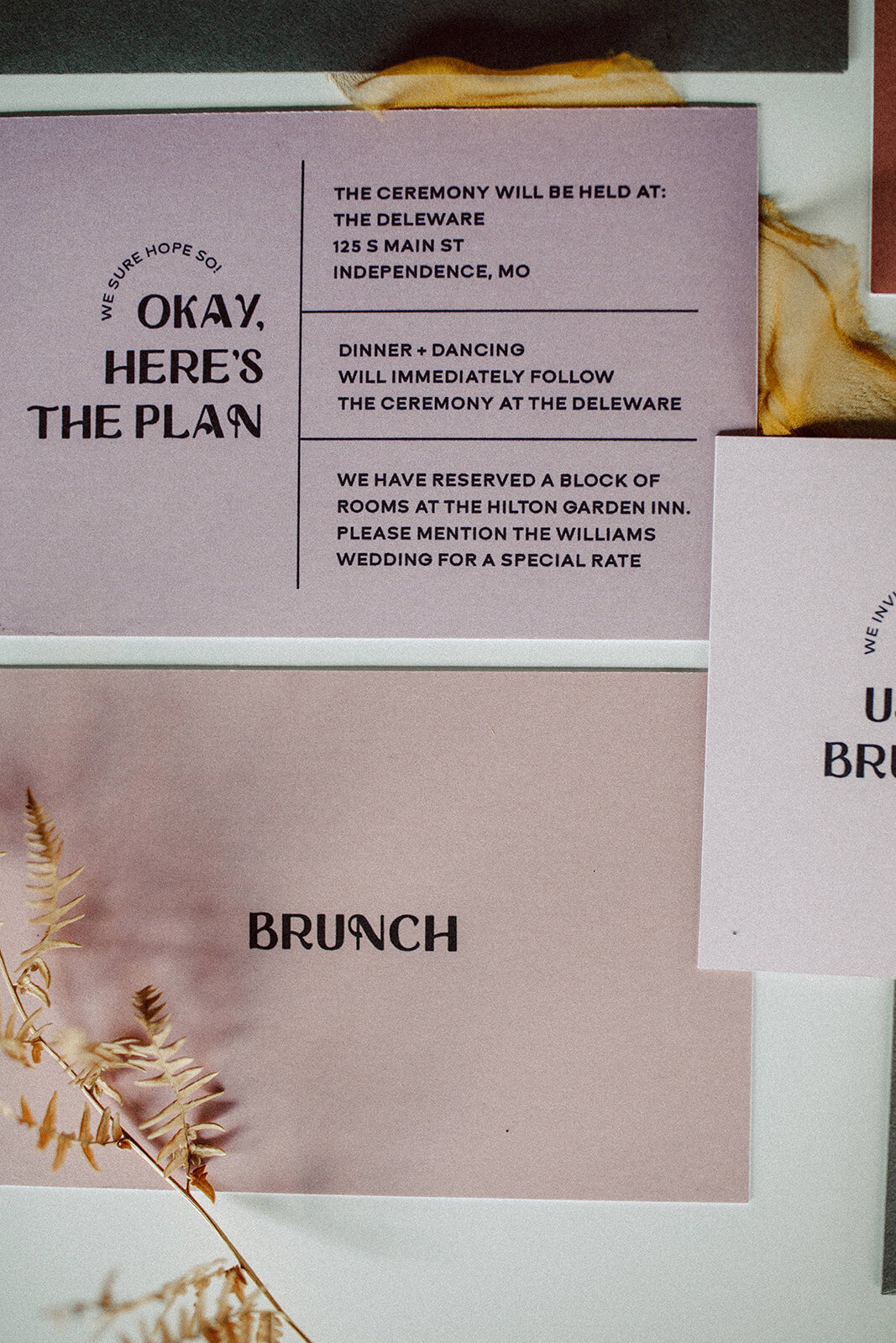 Mauve and blush-colored wedding invitation with black font with white fern stem.