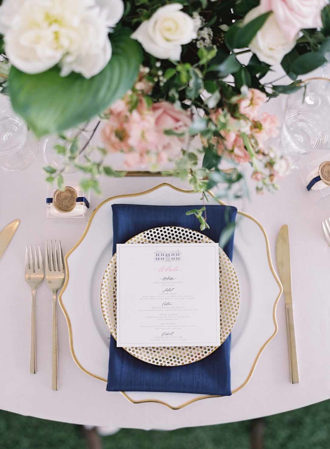 gold rimmed plates with navy napkin and menu card with garden flower centerpiece