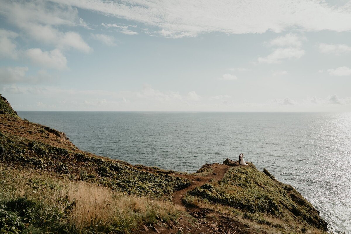 Bride and groom hold hands on a cliffside trail during their Oregon Coast elopement photography adventure