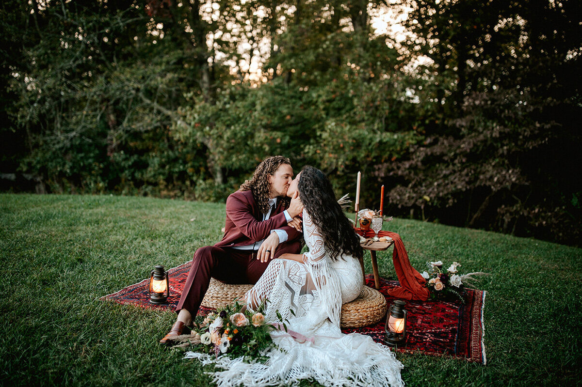 bride and groom wearing a white lace wedding gown and burgundy tuxedo while kissing outdoors