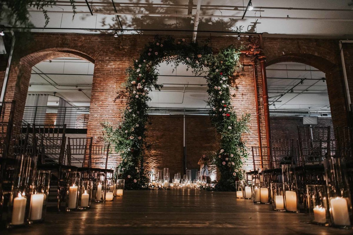 large arch of greenery and blush and red flowers for a wedding ceremony at Axis Pioneer Square with candles lining the aisle