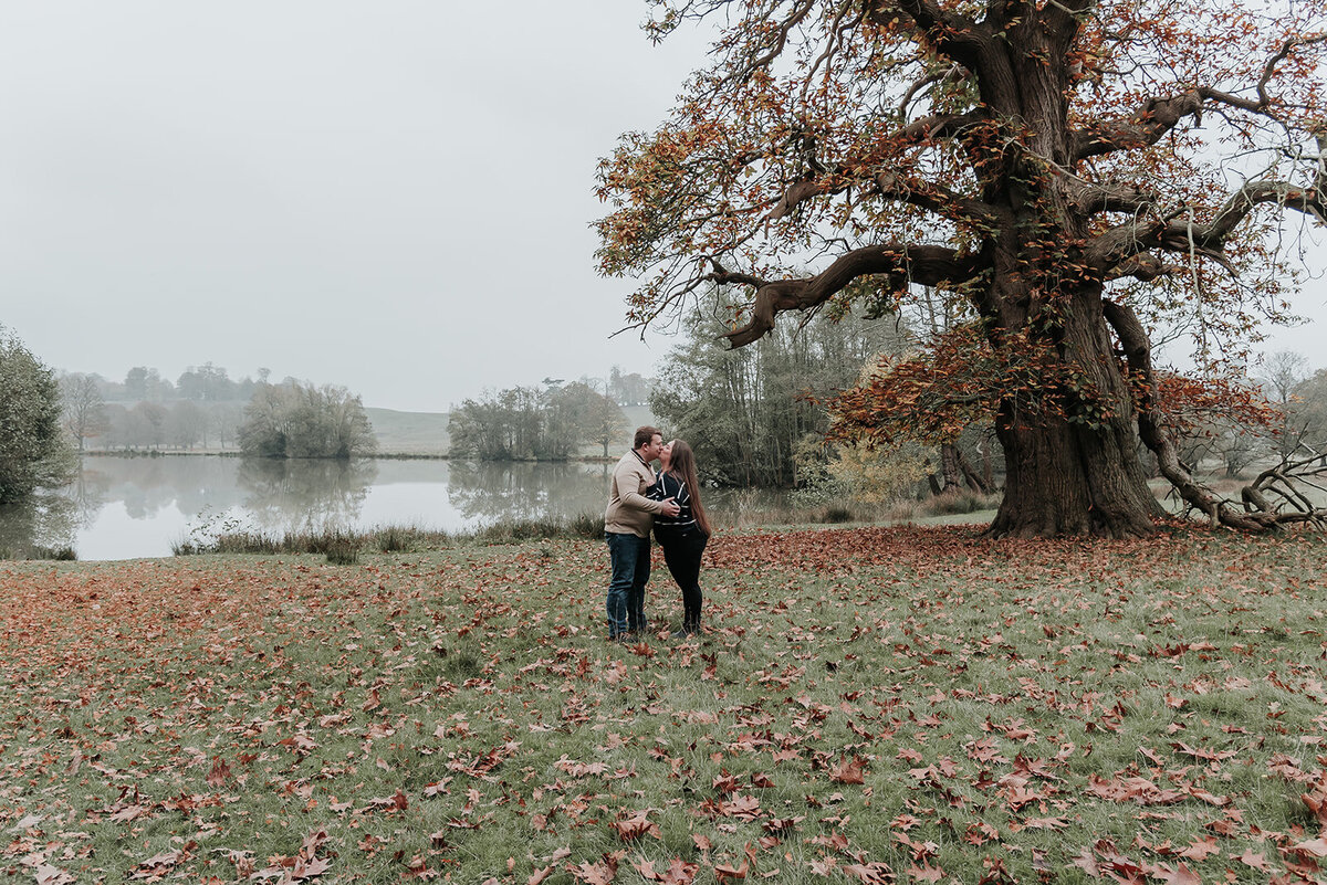 Couple kiss under autumn tree at Petworth Place