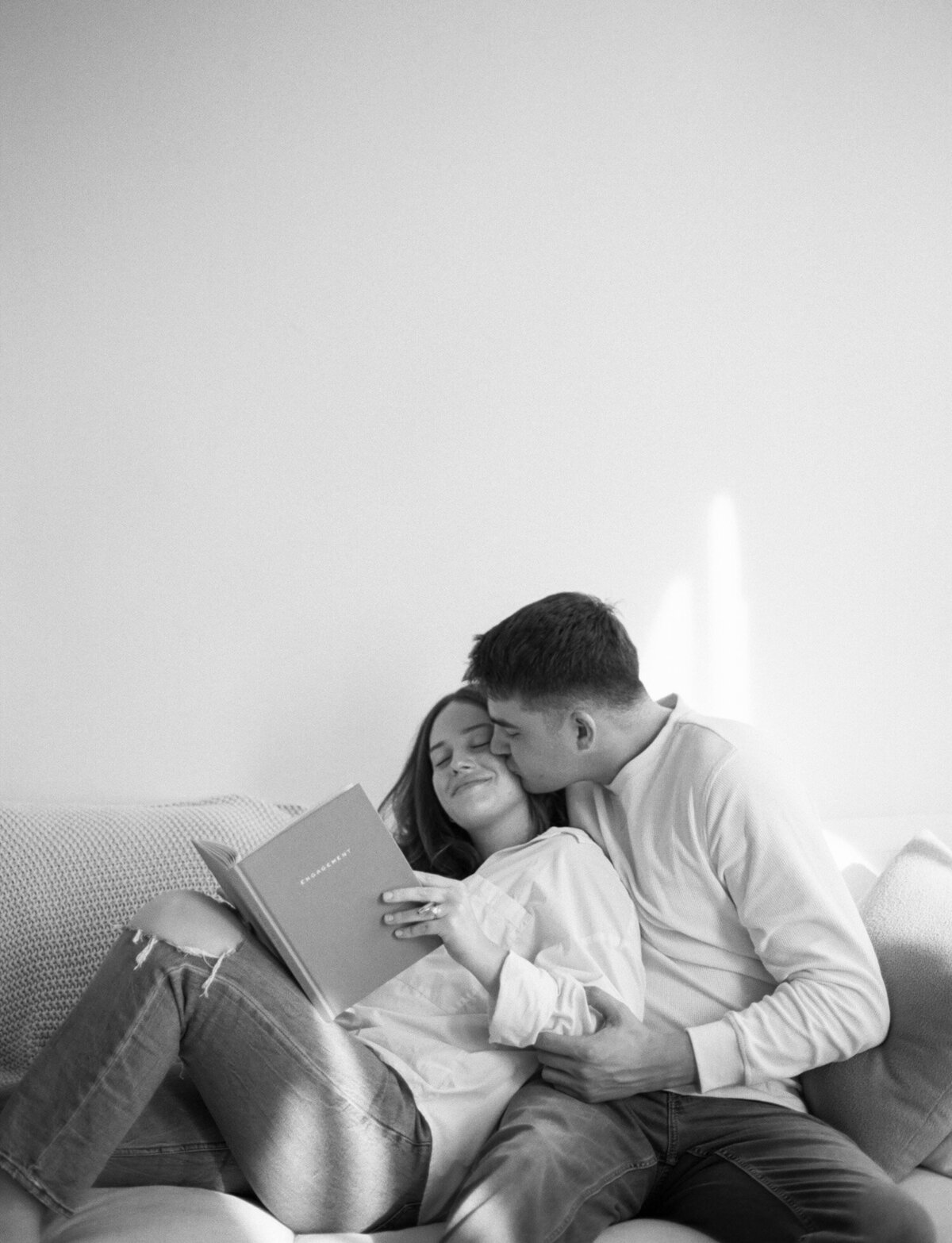 couple embraces while journaling on couch, white natural light studio, Michigan branding photographer