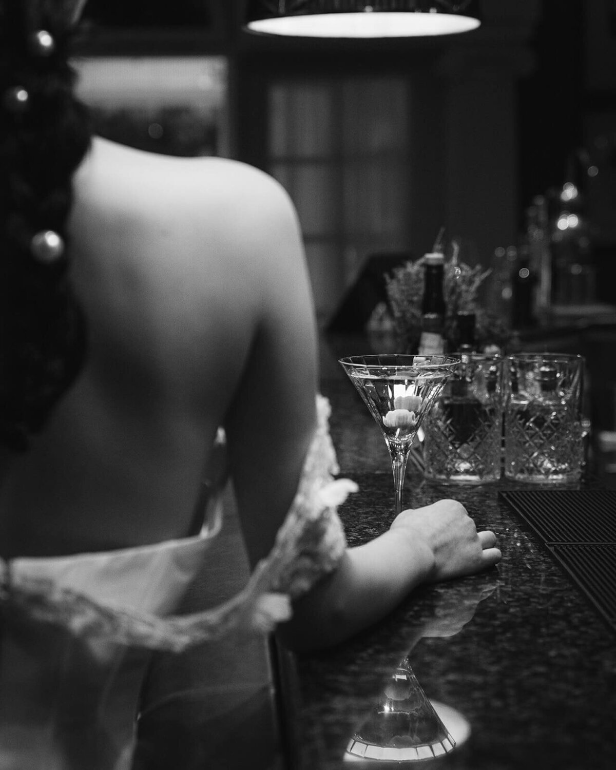 The shoulder of a bride with her dress draped over as she picks up a cocktail glass.