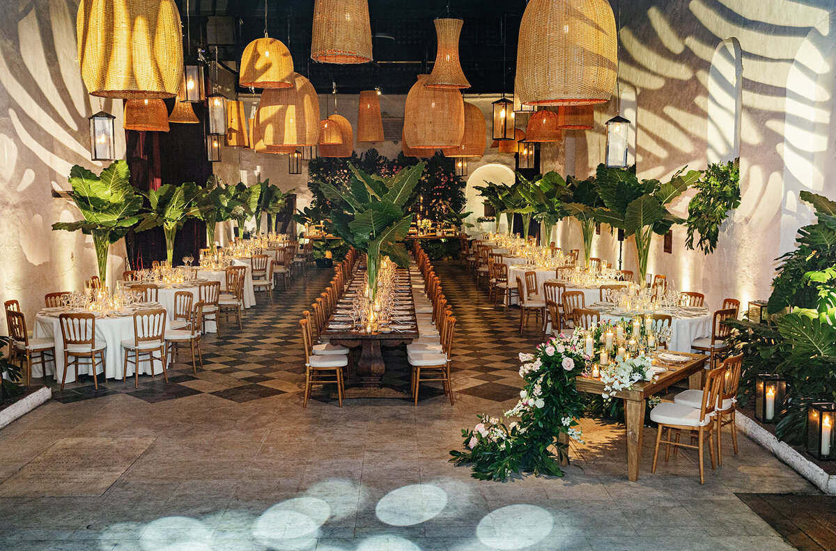 A stunning wedding reception venue in Cartagena, featuring warm hanging lanterns, tropical greenery, and long banquet tables.