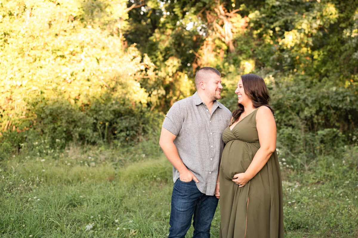 Young expectant parents laughing in a field while mom holds her pregnant belly