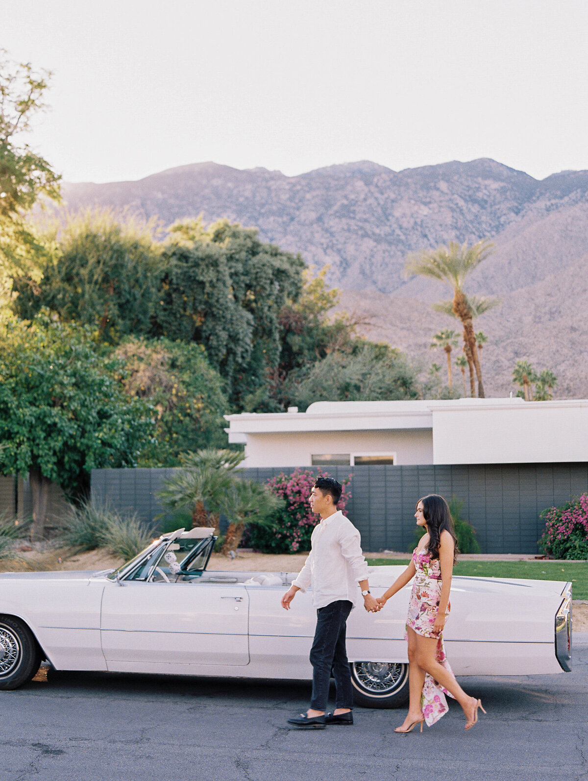 a couple walking hand in hand with a vintage car and the mountains behind them