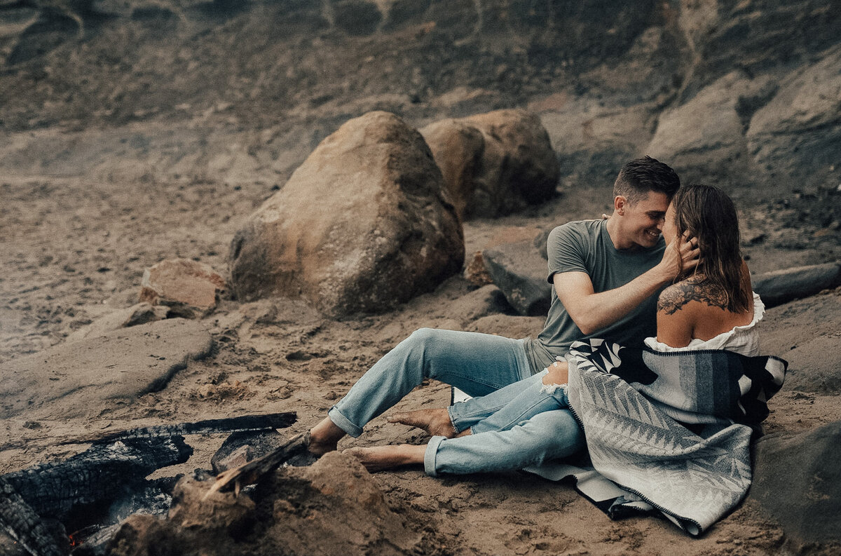 couple sits on a blanket at cape kiwanda next to a fire on the beach