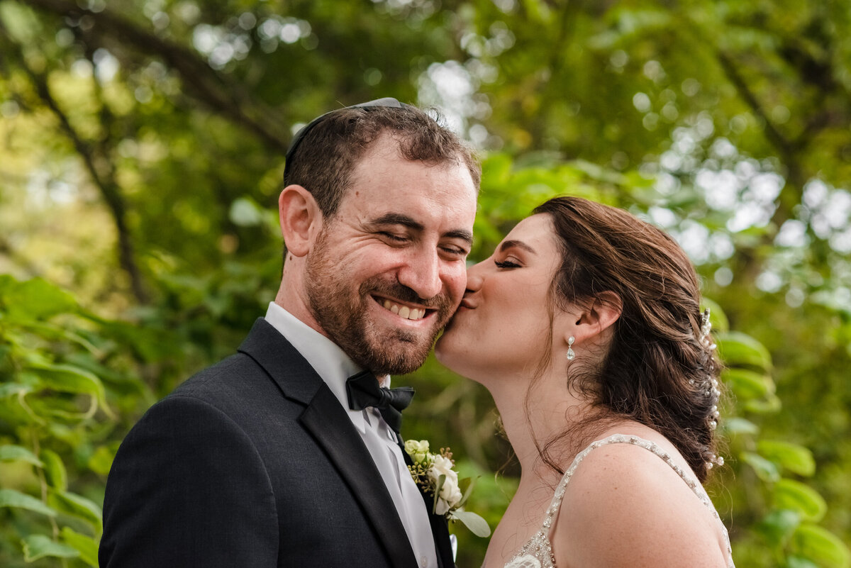 Bride kisses the cheek of the groom in the woods
