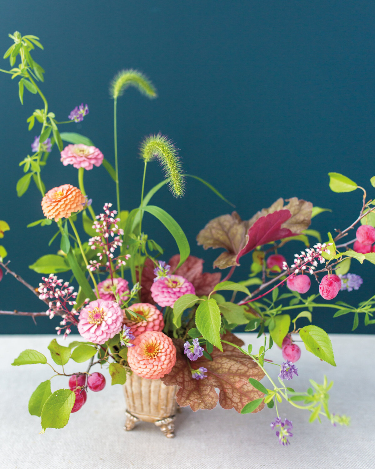 A floral arrangement of bright flowers and organic greenery in a small, square pot.