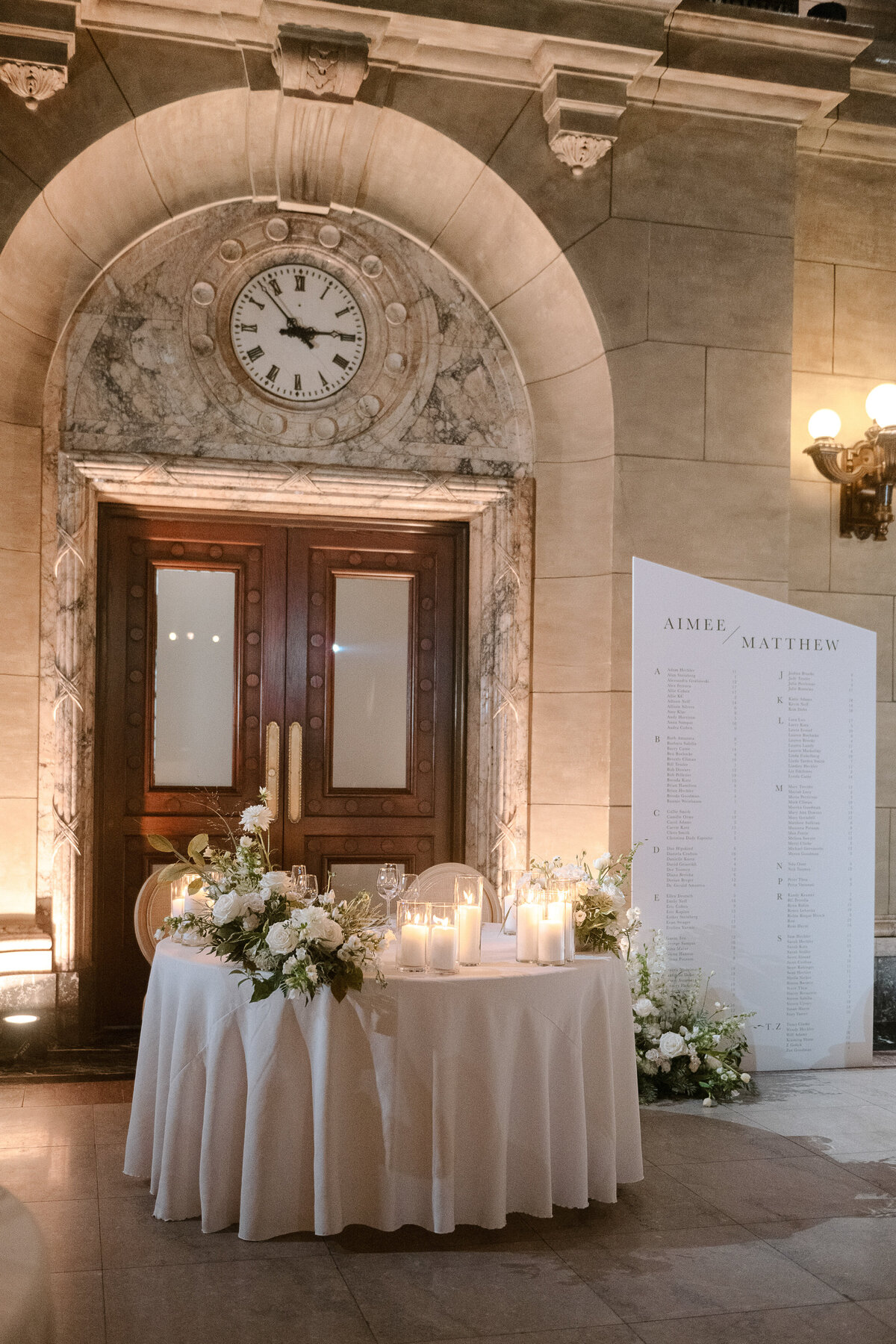 A sweetheart table at Theatre St James is decorated with white flowers in front of a marble wall. 