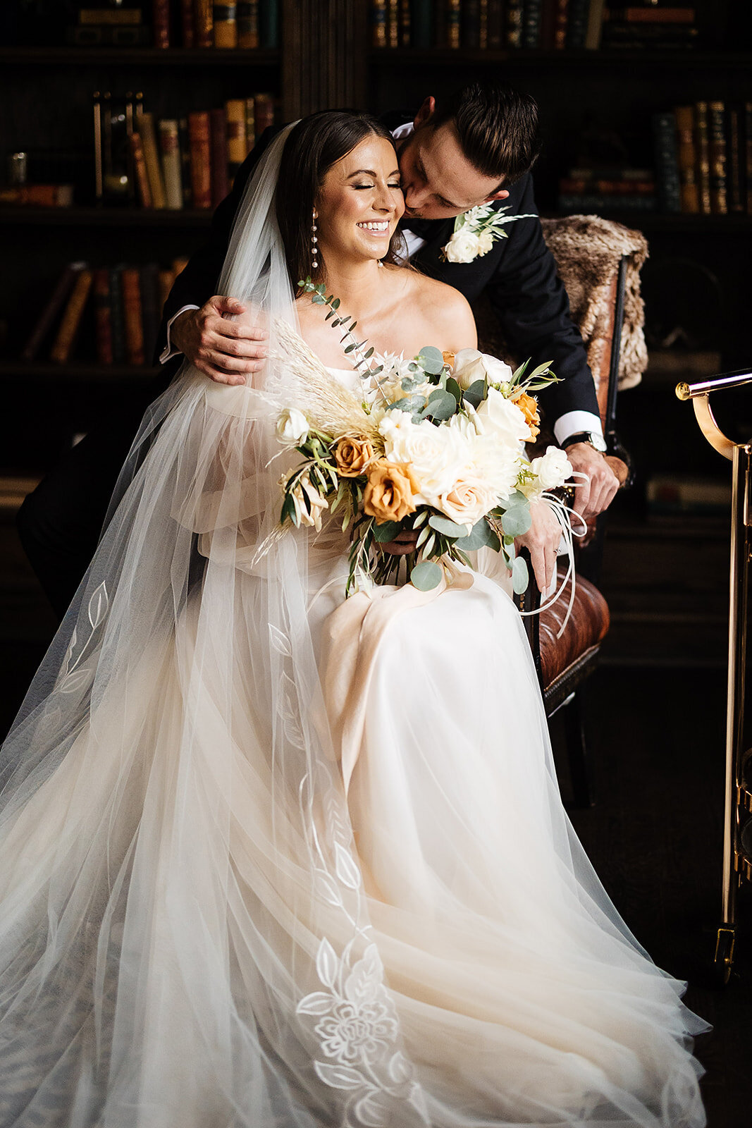 Bride and groom on their wedding day  in a library  with an orange, tan, and white boho floral bouquet.