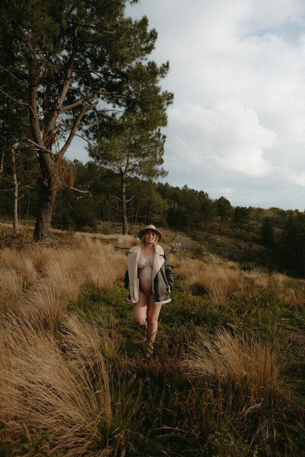 Femme enceinte en sous-vêtements marchant dans les hautes herbes, blouson aviateur et chapeau de feutre. Séance photo grossesse en Bretagne par Kamescop.