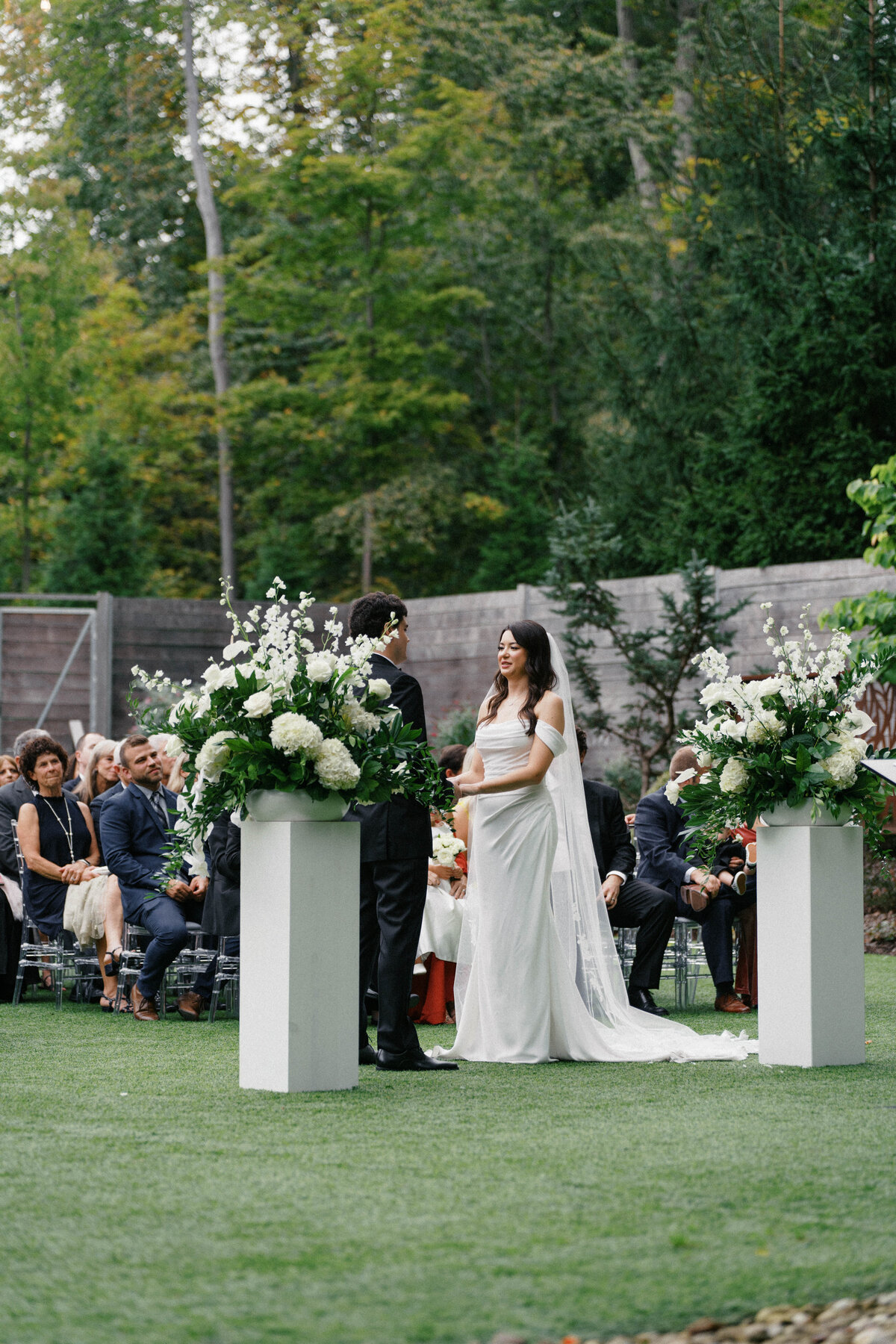 Bride and groom exchange vows outdoors at Sapphire Creek Winery, surrounded by lush greenery and floral arrangements.

