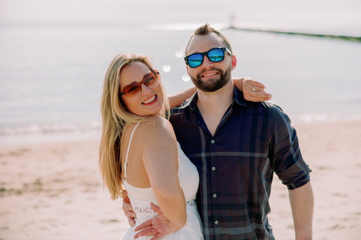 A couple with their arms around each other smiling with sunglasses on 