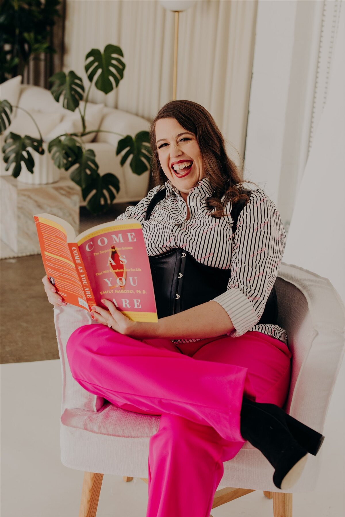 woman sitting in a chair holding come as you are book while smiling