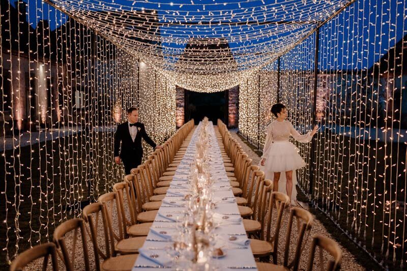 Mariés découvrant leur salle de repas en extérieur, illuminée par un toit de guirlandes LED au Carré de Lailly.