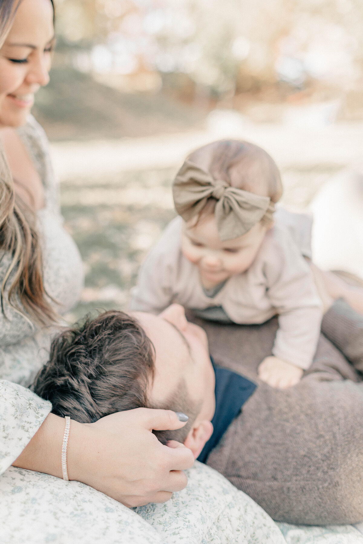 Mom, dad, and baby girl laying down on a blanket smiling and snuggling during a relaxed Kansas City first birthday session