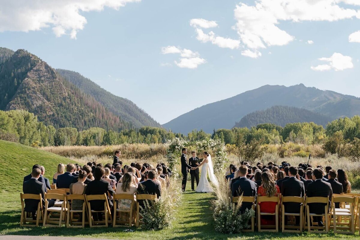 Wide view of the wedding ceremony at Aspen Meadows Resort, with the couple exchanging vows surrounded by scenic mountain views.