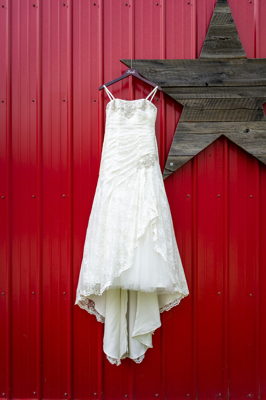 The brides dress hanging on a wooden star on the outside of a red barn.
