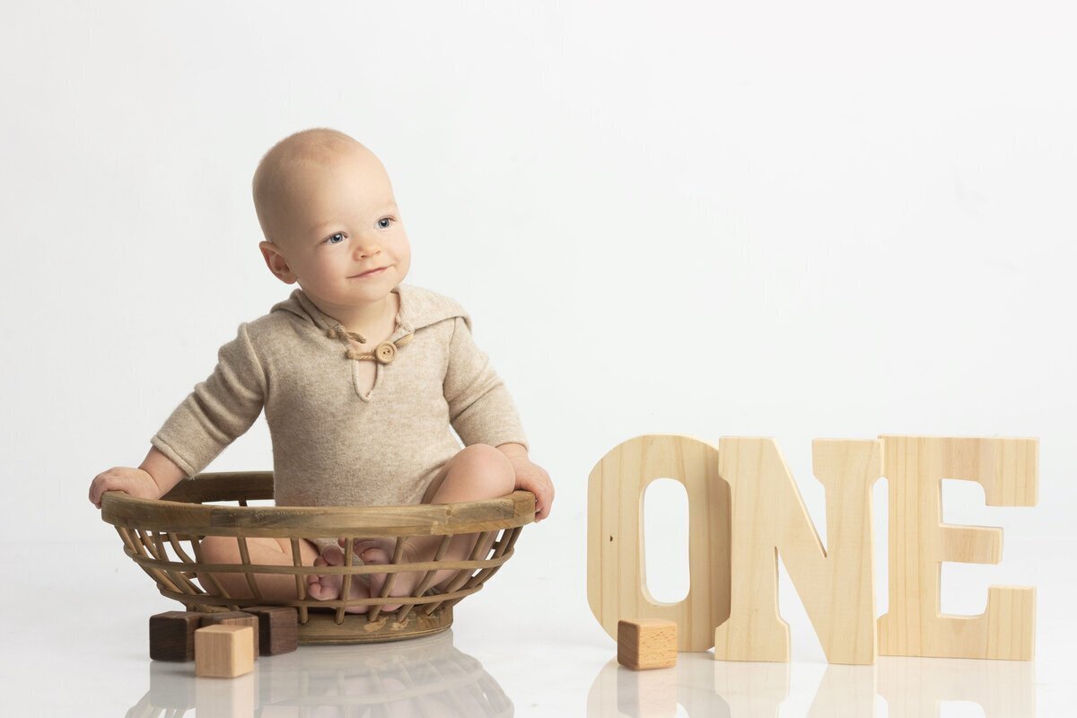 Baby sitting in basket next to one year old sign, taken by new jersey photographer Ally Kimpton Photography