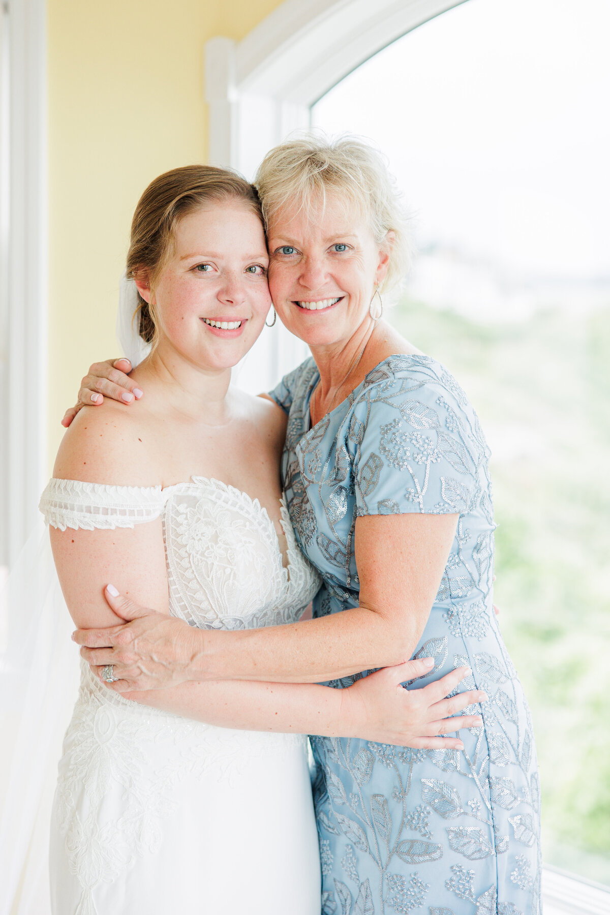 Bride hugging her mom and looking at the camera representing family moments during a Boston wedding