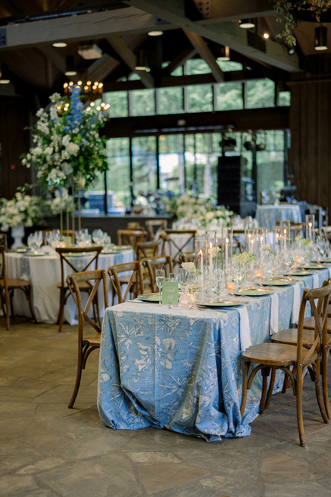 Long reception table with white and soft blue florals, tapered candles, and layered place settings.”

