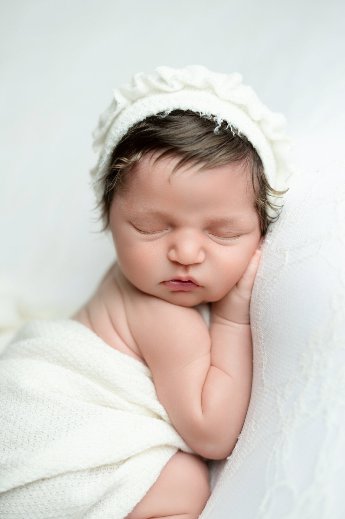 Close-up newborn girl with floral headband in soft white setup.