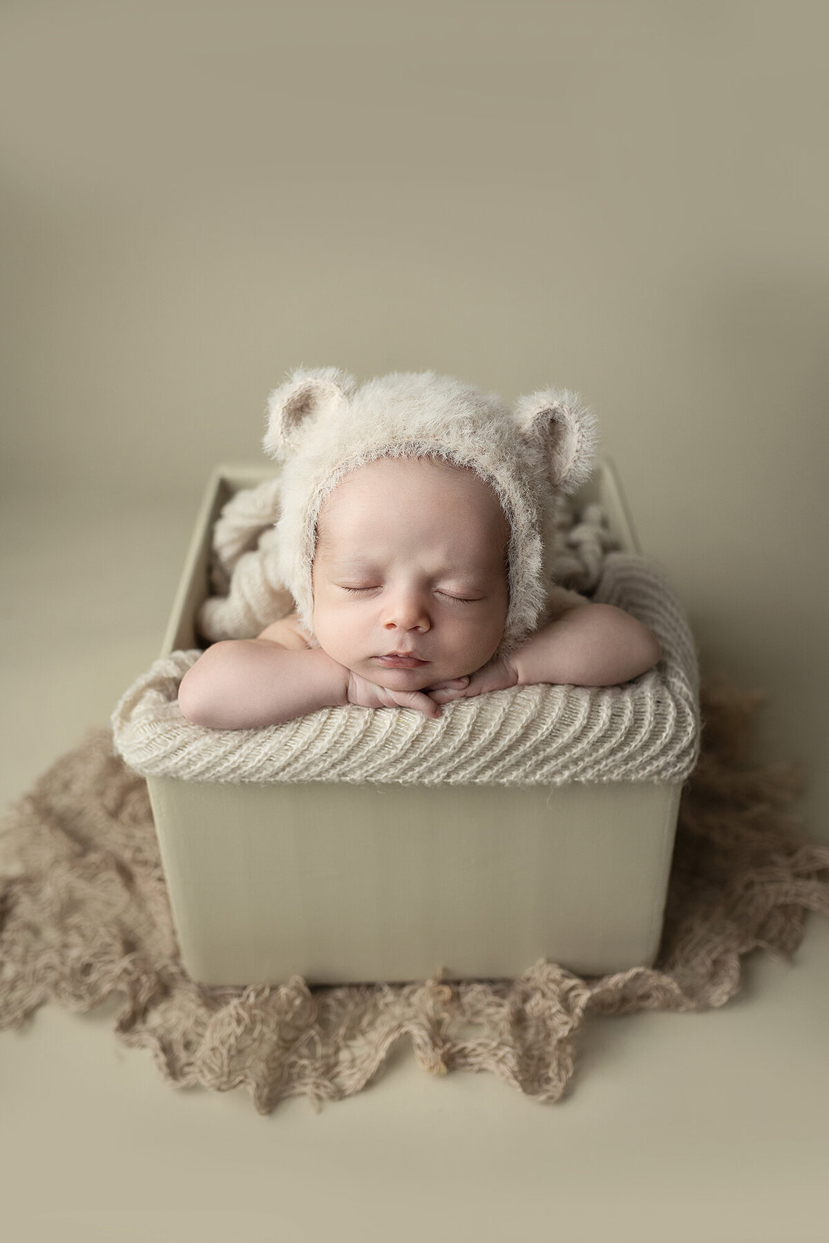 Baby boy posed in box wearing a bear bonnet.
