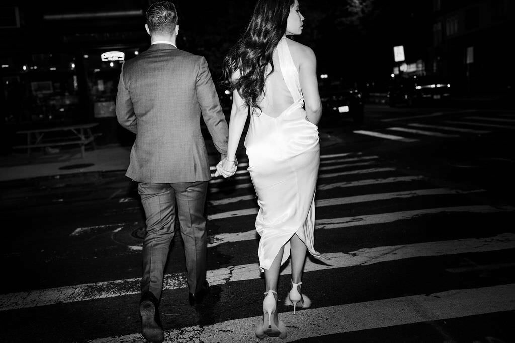 black and white photo of a couple holding hands and walking across a city street together