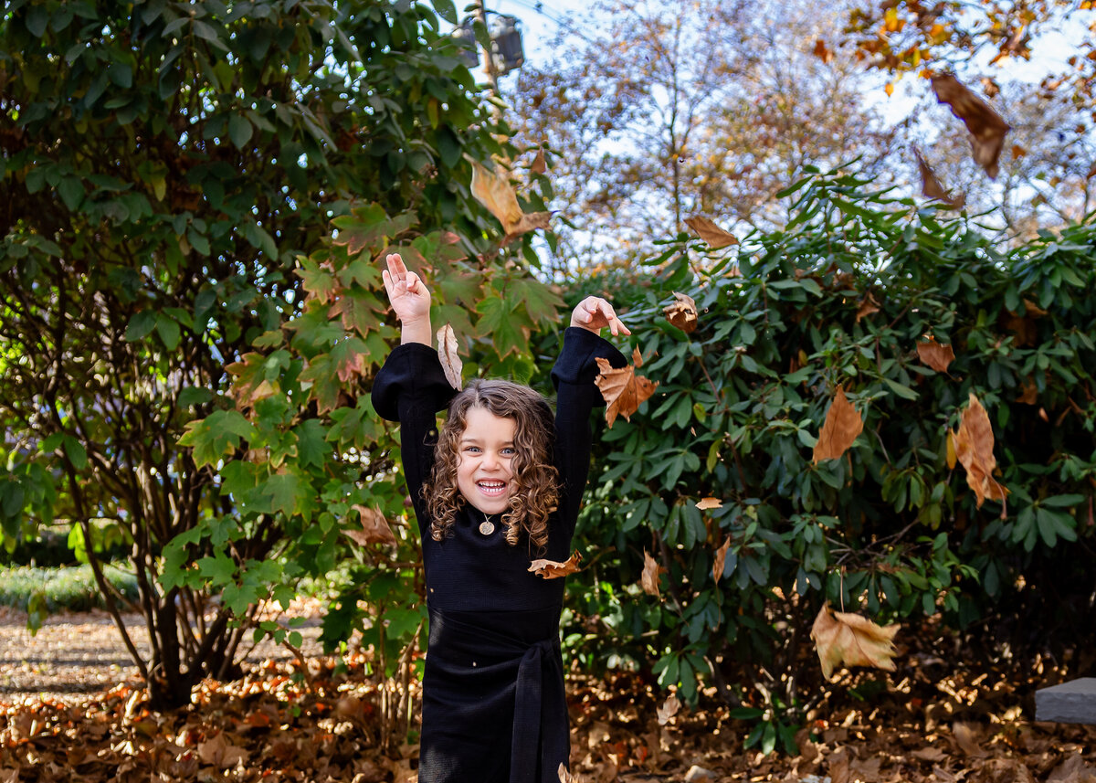 Lifestyle photo of girl throwing fall leaves at an Essex County, New Jersey park.