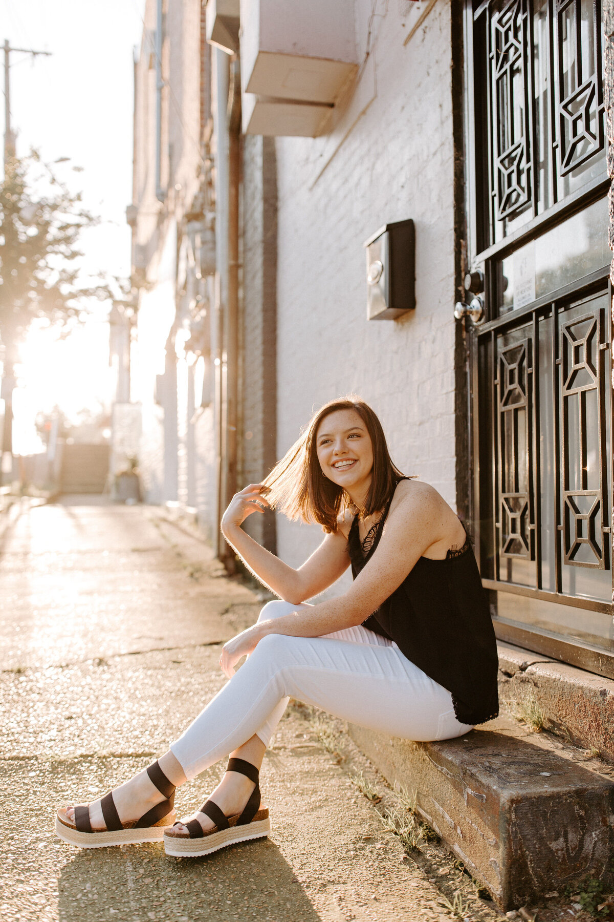 High school senior sitting on the step in front of a door on a downtown sidewalk