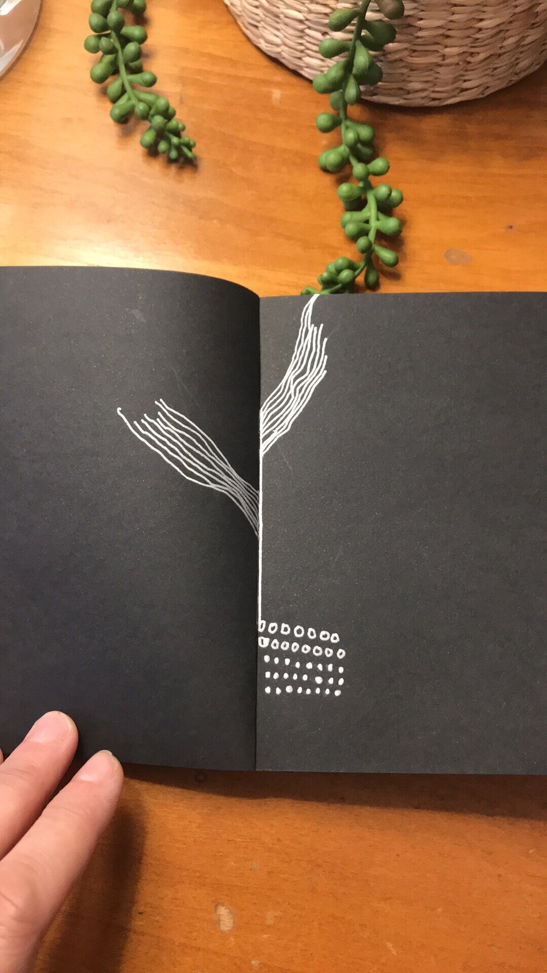 A hand holding open an art journal with abstract line drawings.