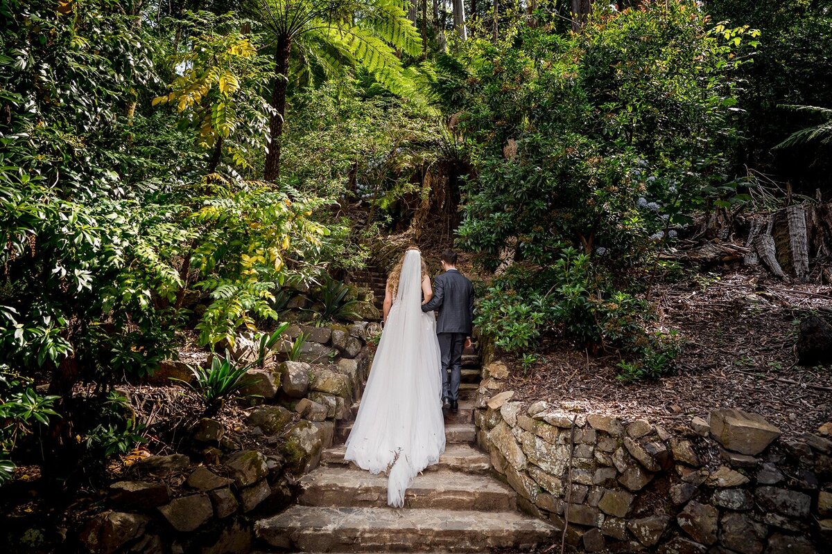 A bride and groom standing on rocks with the tide out and a beautiful sunset with scattered clouds
