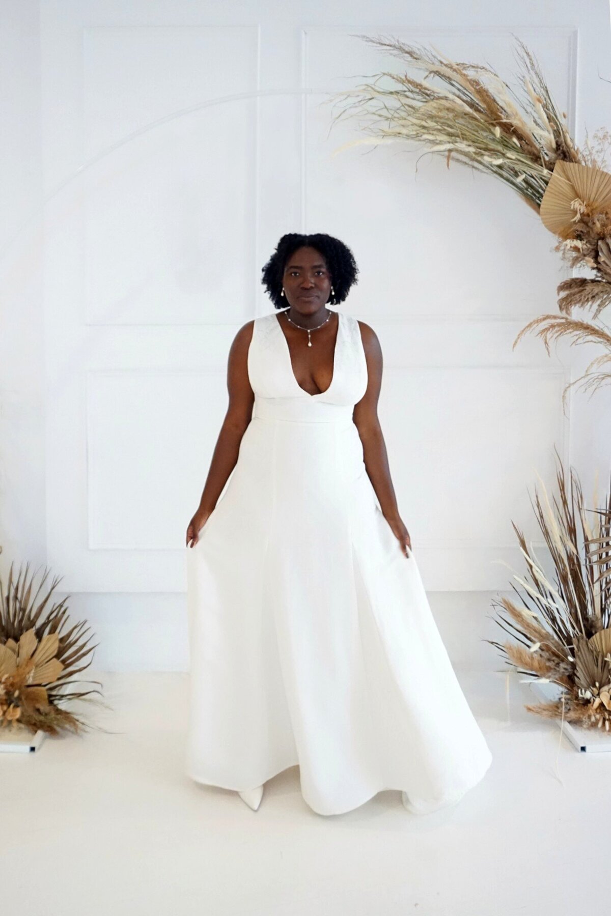 Black model in a v-neck, modified a-line wedding dress. The floral pattern of the crepe fabric climbs the skirt from the hem.