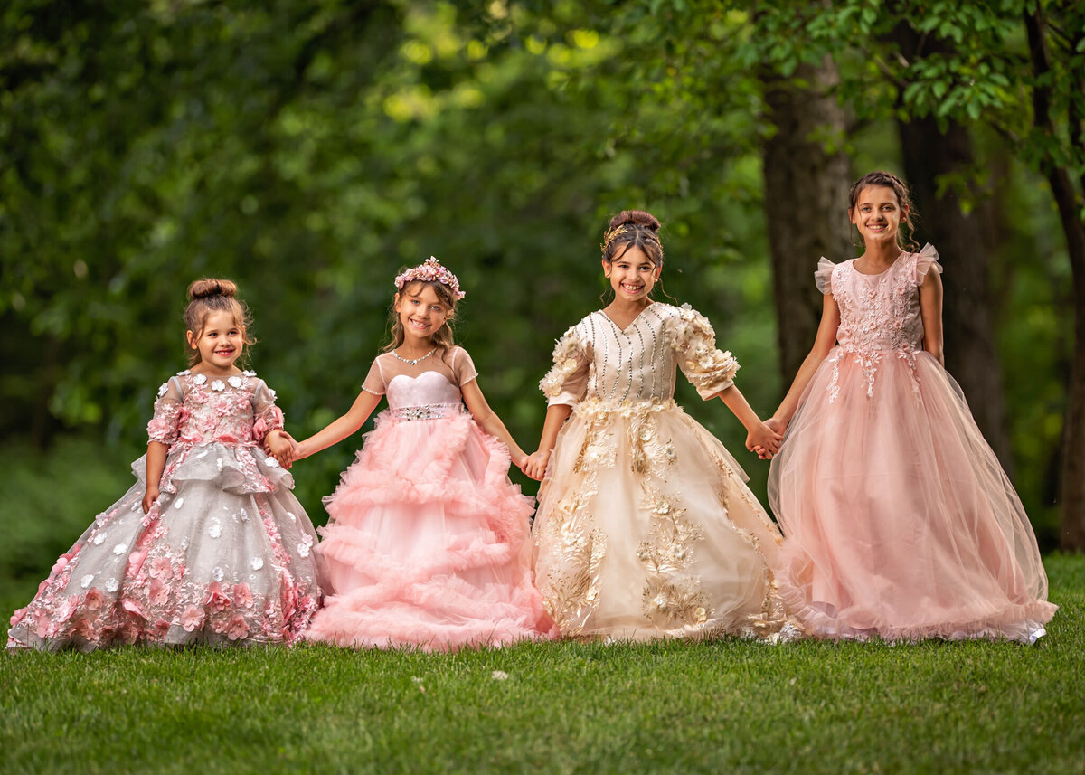 Elegant outdoor portrait of four young girls dressed in stunning princess gowns, posing together in a lush green setting. Captured in Leawood, Kansas, this regal group setup is perfect for families seeking formal and memorable child photography