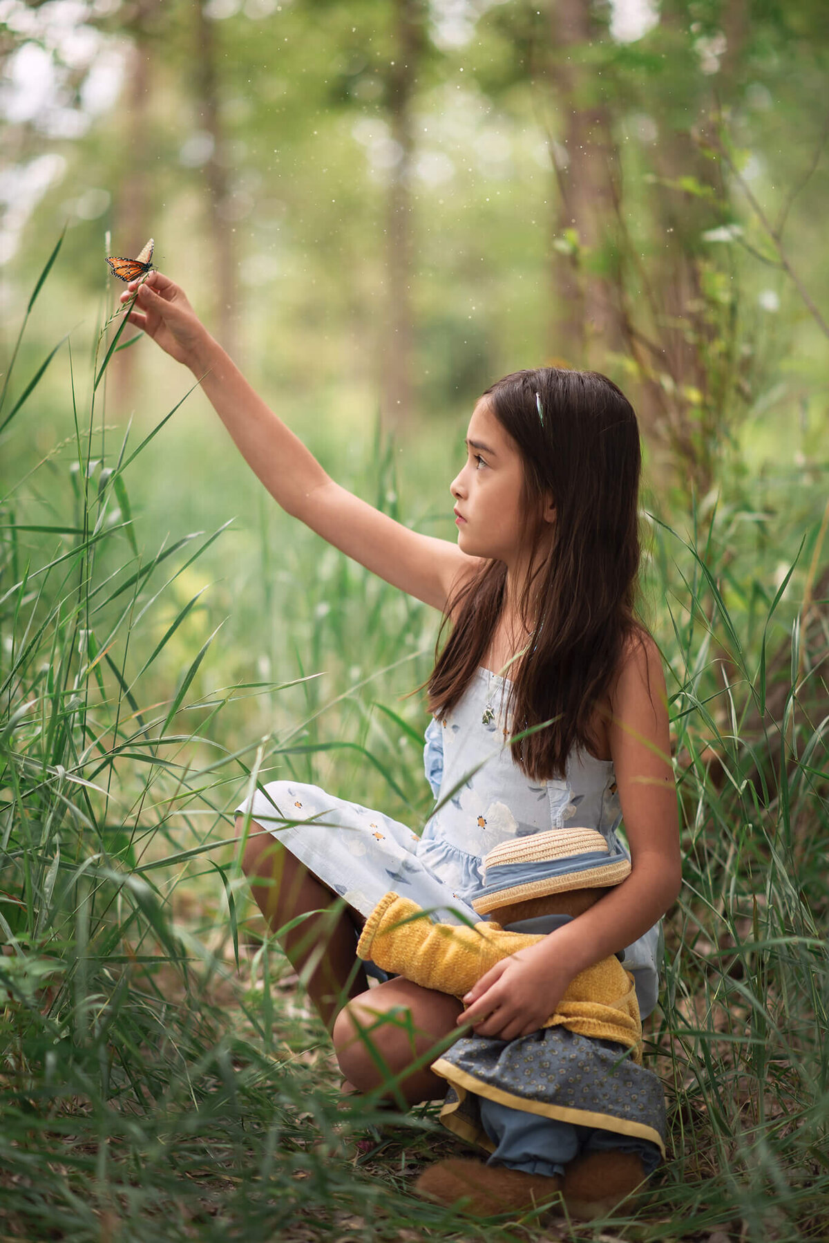 Springtime in Kamloops fetaures a little girl crouched in the tall grass while holding her hand up on a piece of grass while a butterfly lands on her.  Beautiful portrait by Brittany Danielle