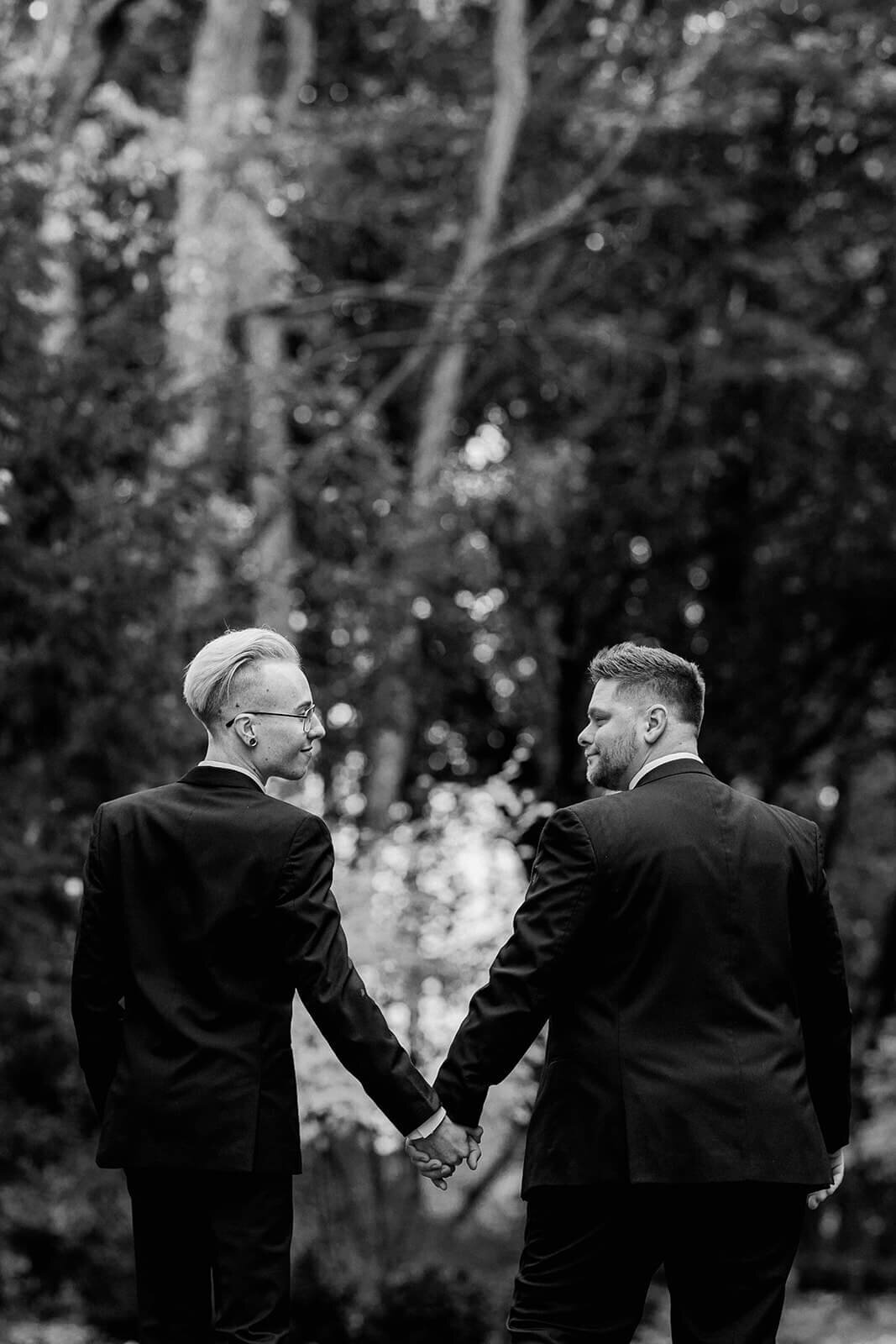 two grooms in suits holding hands and looking at each other