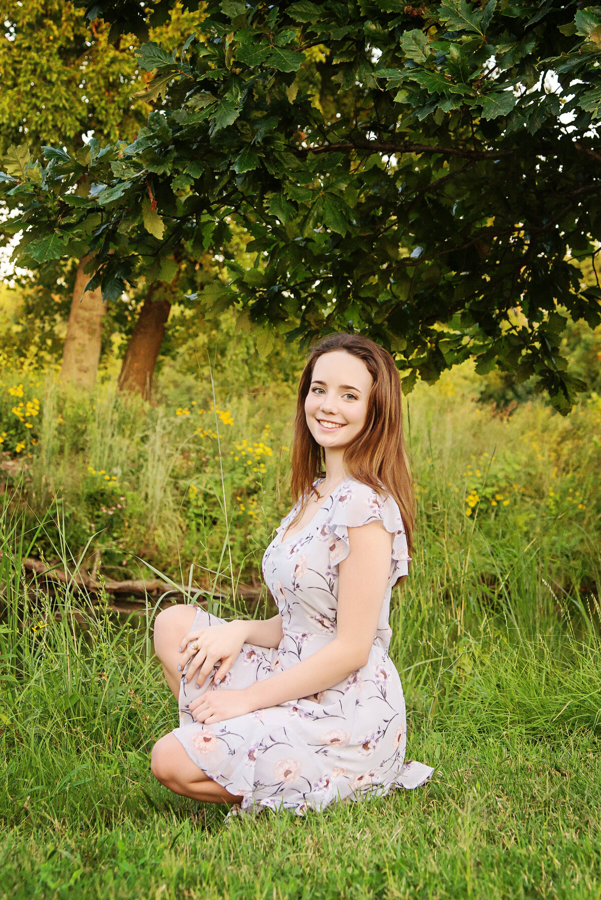 st-louis-senior-photographer-senior-girl-kneeling-in-dress-in-front-of-tall-grass-in-forest-park