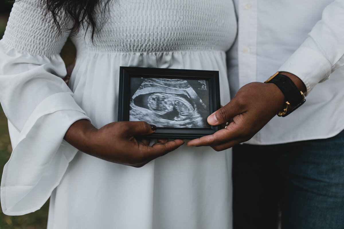 Maternity shot with soon to be mom, and dad kissing holding ultra sound photo.