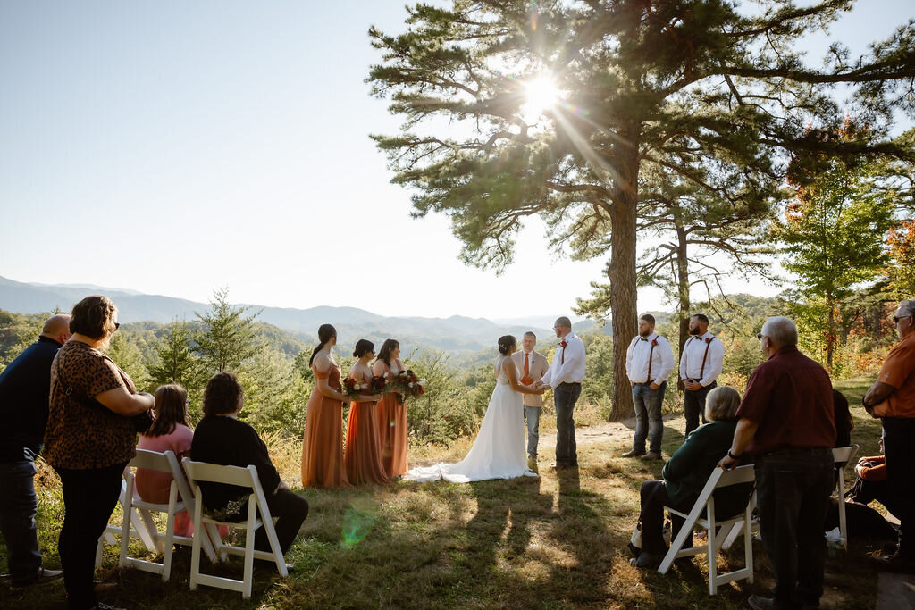 Foothills Parkway ceremony with couple getting married under a tree on an outlook with their guests in white wooden chairs captured by Gatlinburg photographers 