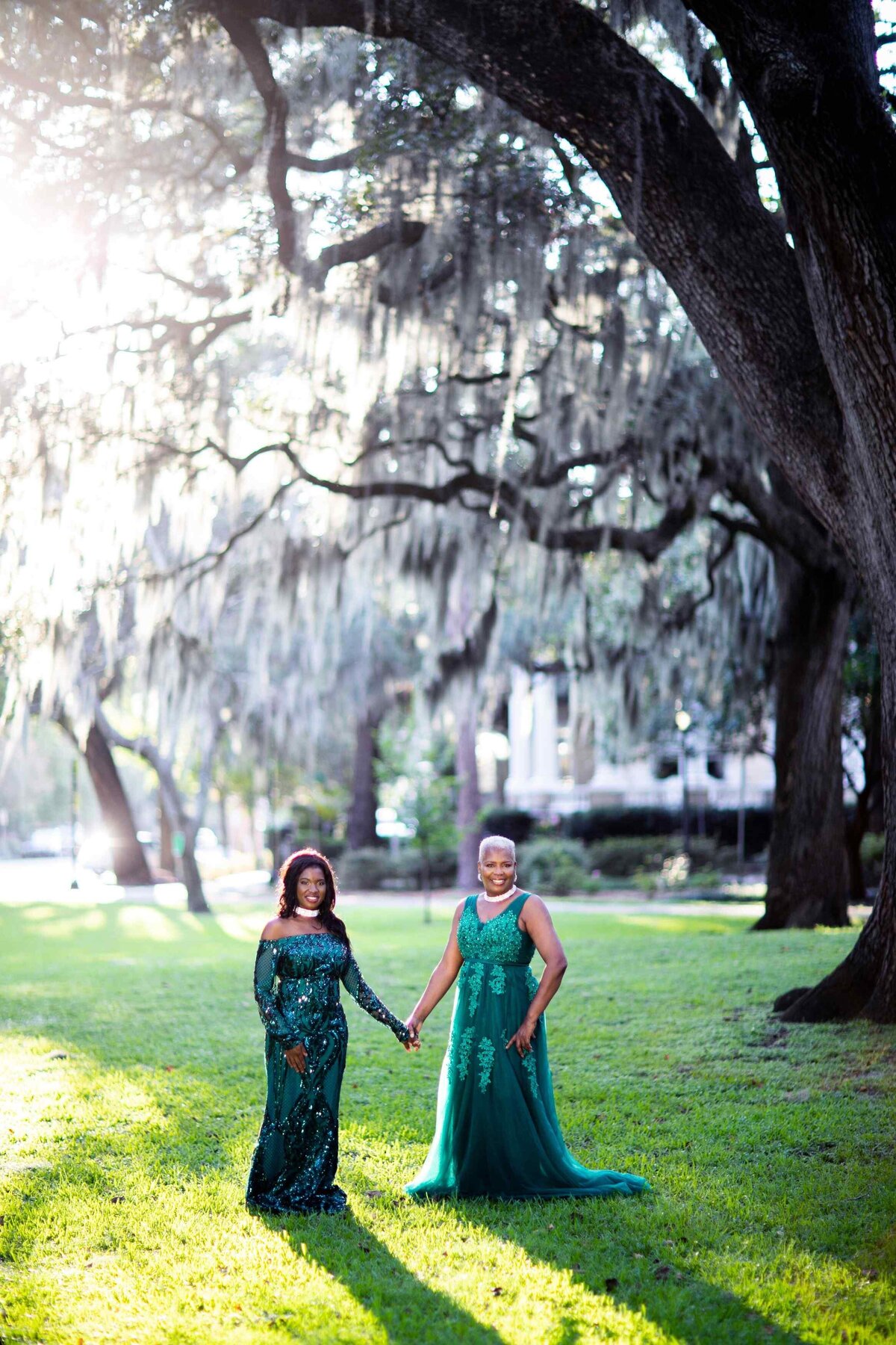 two women holding hands posed in gowns under tree