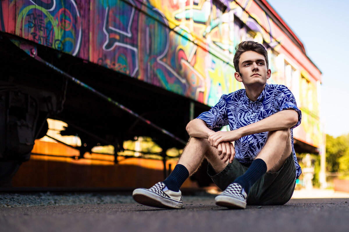 a handsome brown haired senior boy sits near a colorful train car downtown Pittsburgh.