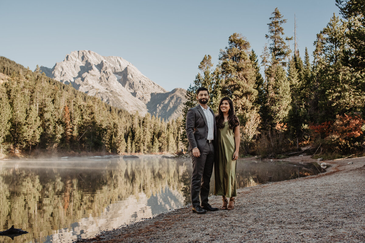Jackson Hole engagement session in the fall with man and woman dressed in formals in front of a lake and mountain in the woods