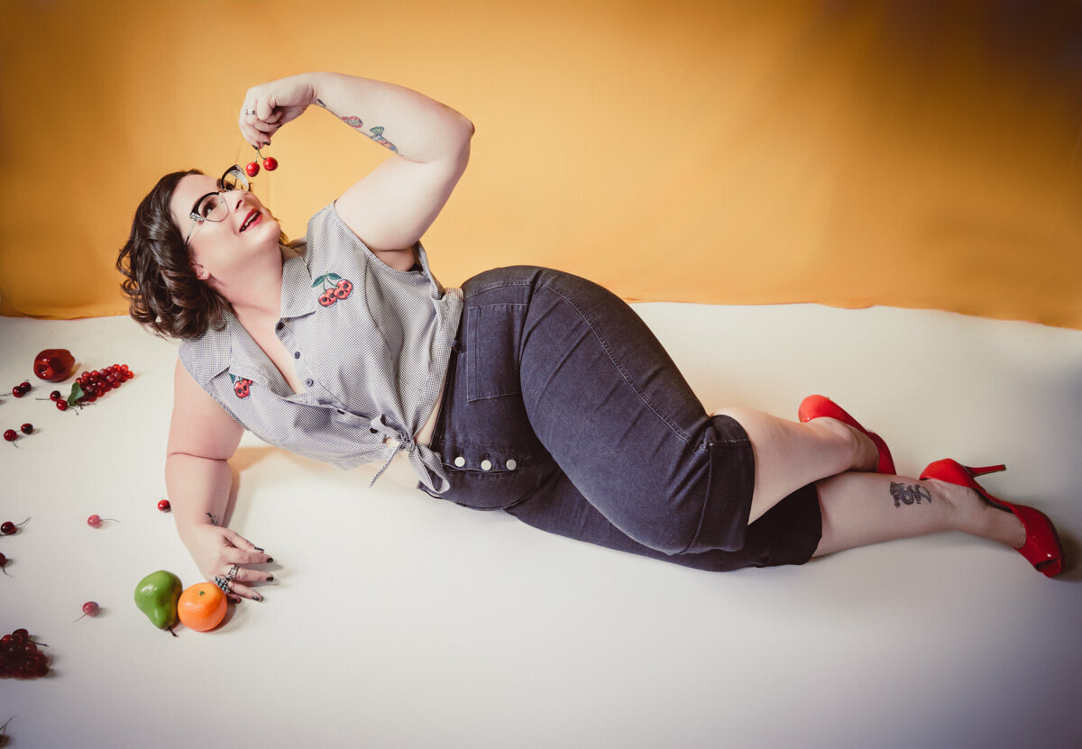 Pinup girl in jeans and crop top laying on her side eating cherries