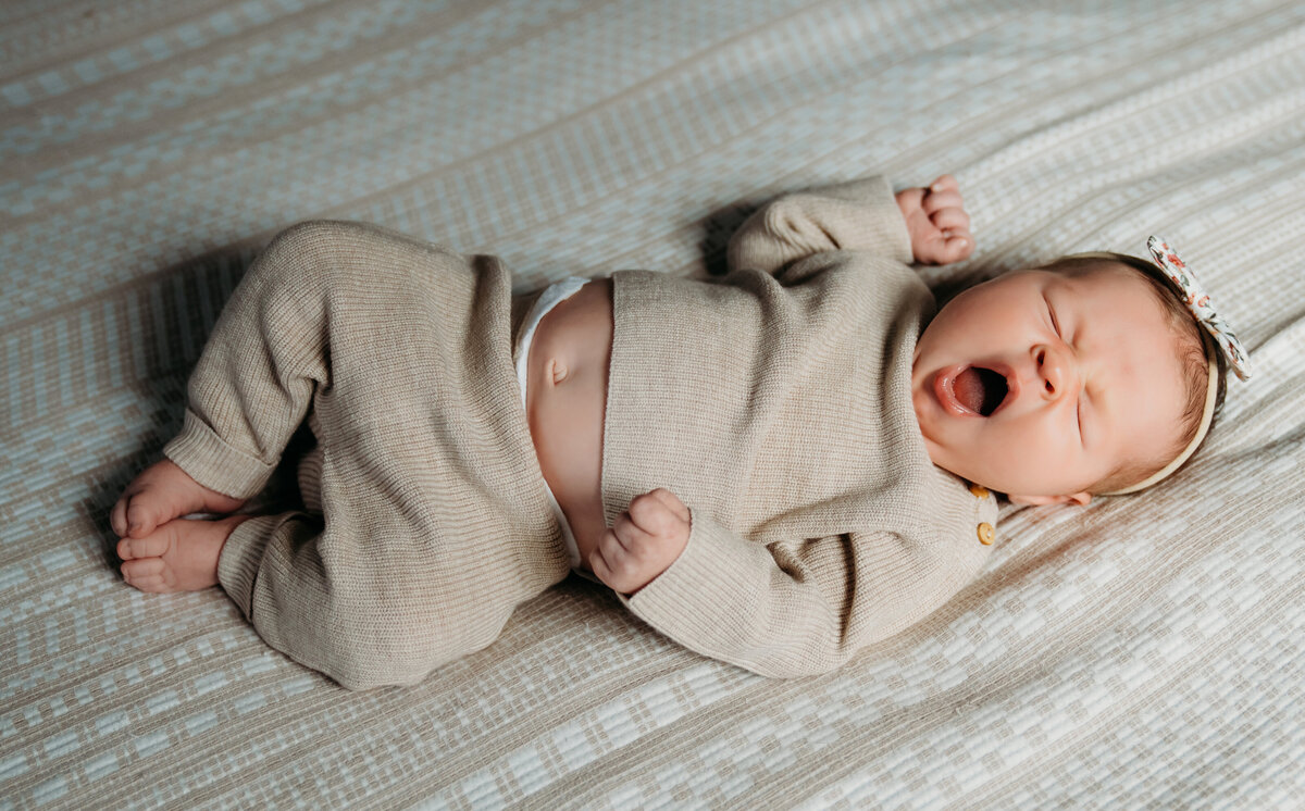Newborn Photographer, a baby lays on a bed and gives a big yawn