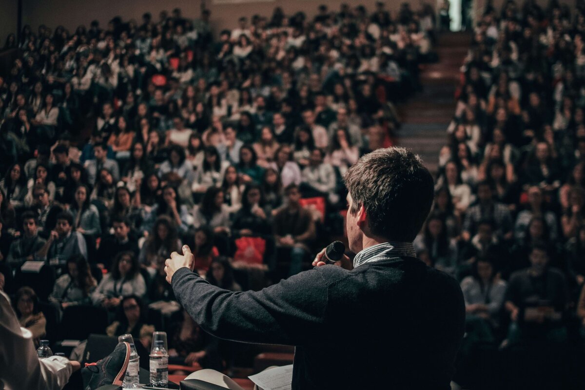 Image of a speaker from behind addressing a crowd from the stage 