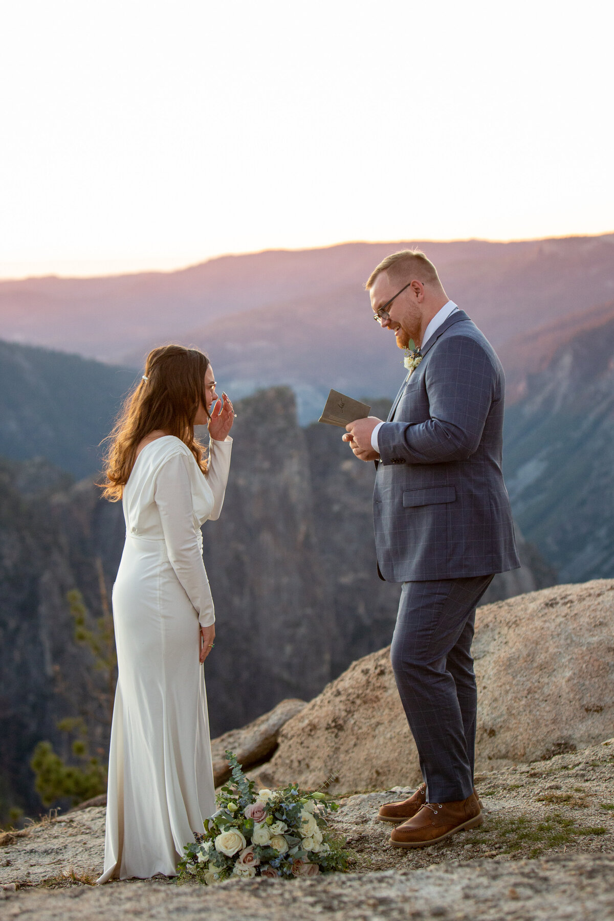 A bride stifles a laugh  as her groom reads his vows to her during their elopement ceremony in Yosemite.
