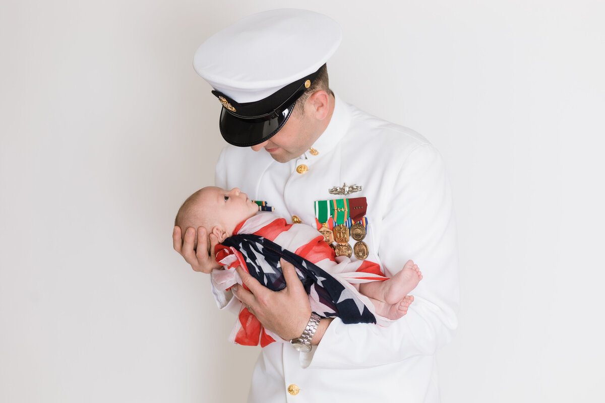 Newborn Photographer, a serviceman holds baby wrapped in flag